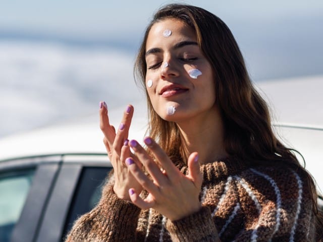 woman applying a sunscreen on her face in snowy mountains in winter 1