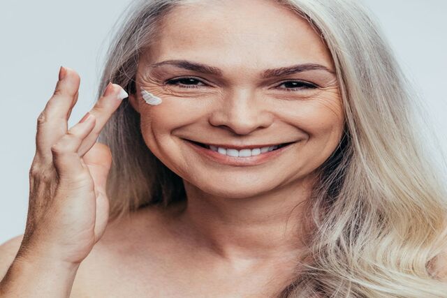 Smiling mid adult caucasian woman applying anti aging cream on her face